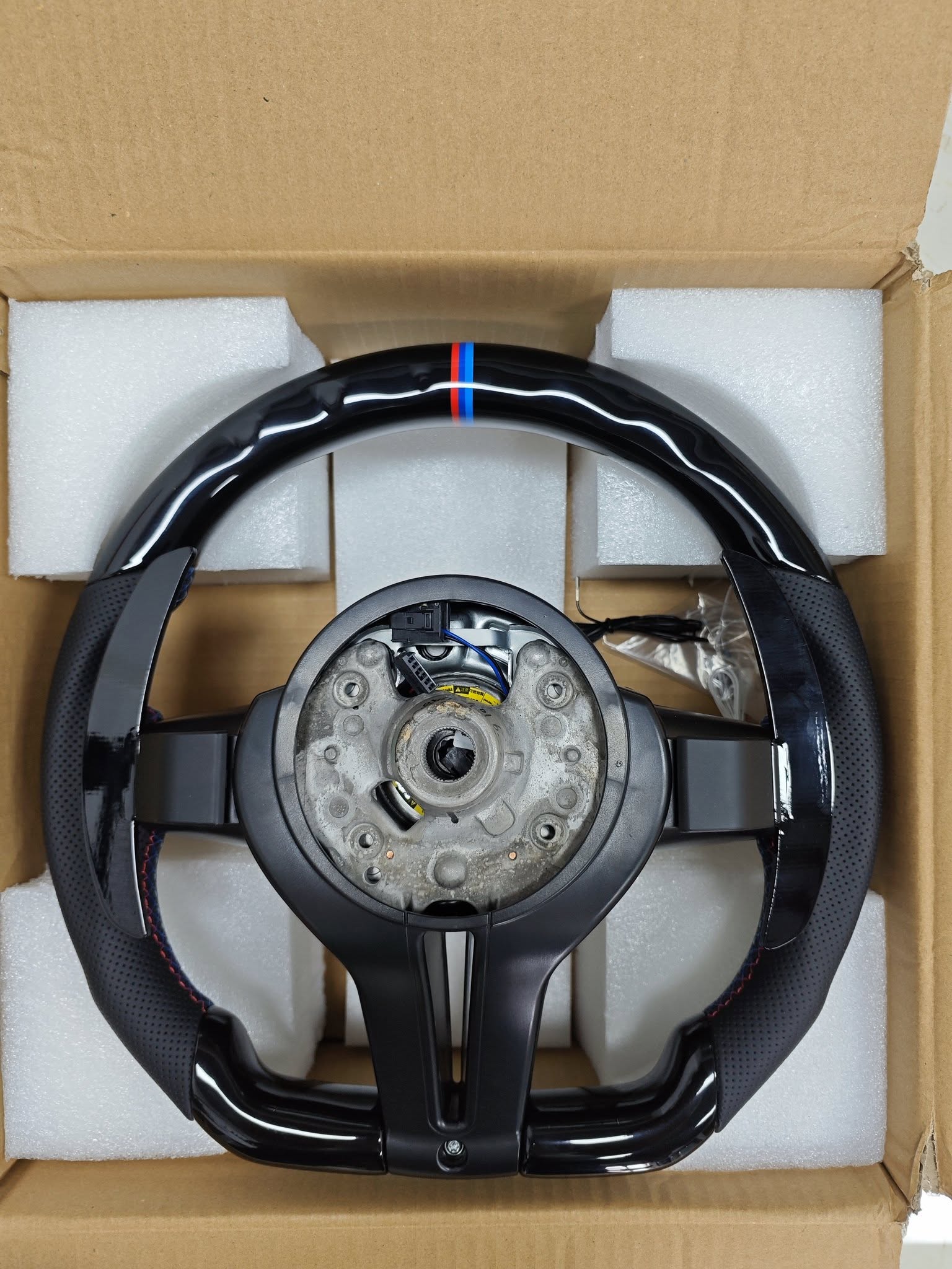 BMW carbon fiber steering wheel with M stripe in protective foam packaging inside a cardboard box