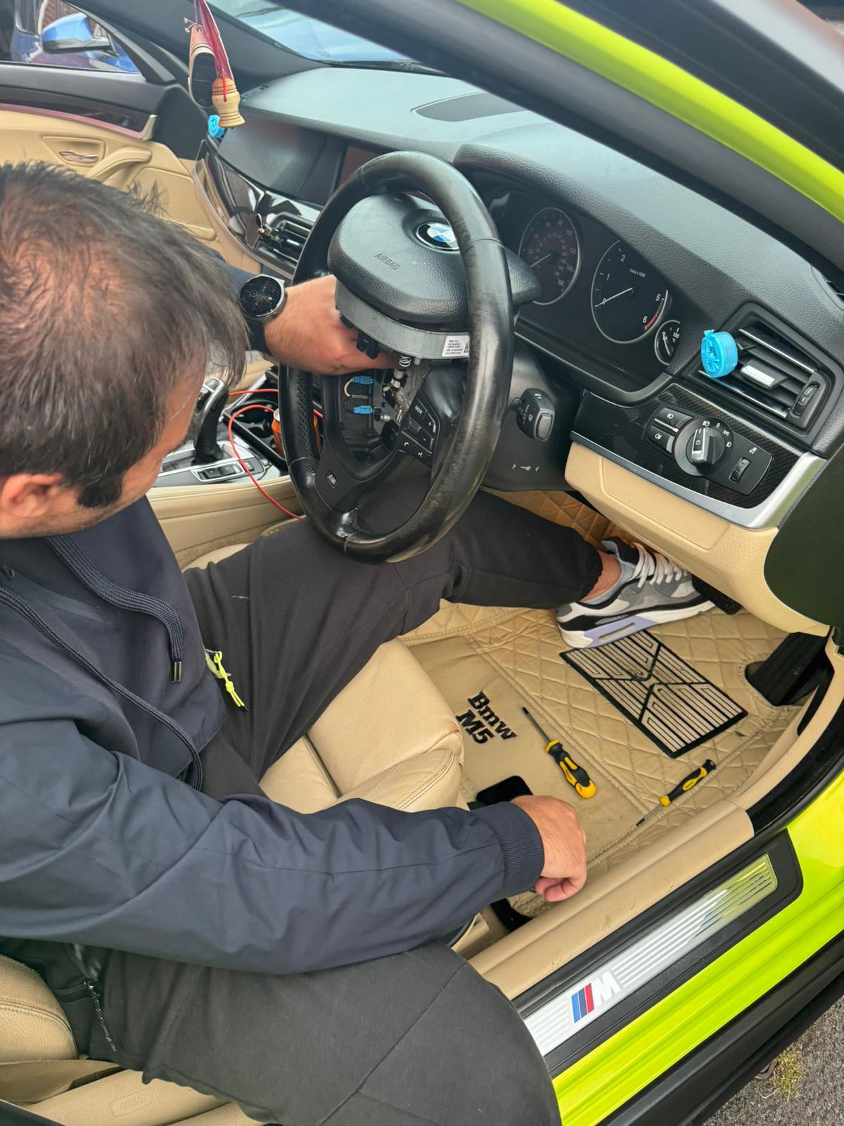 Person installing a custom M series steering wheel in a BMW car with beige interior and detailed dashboard