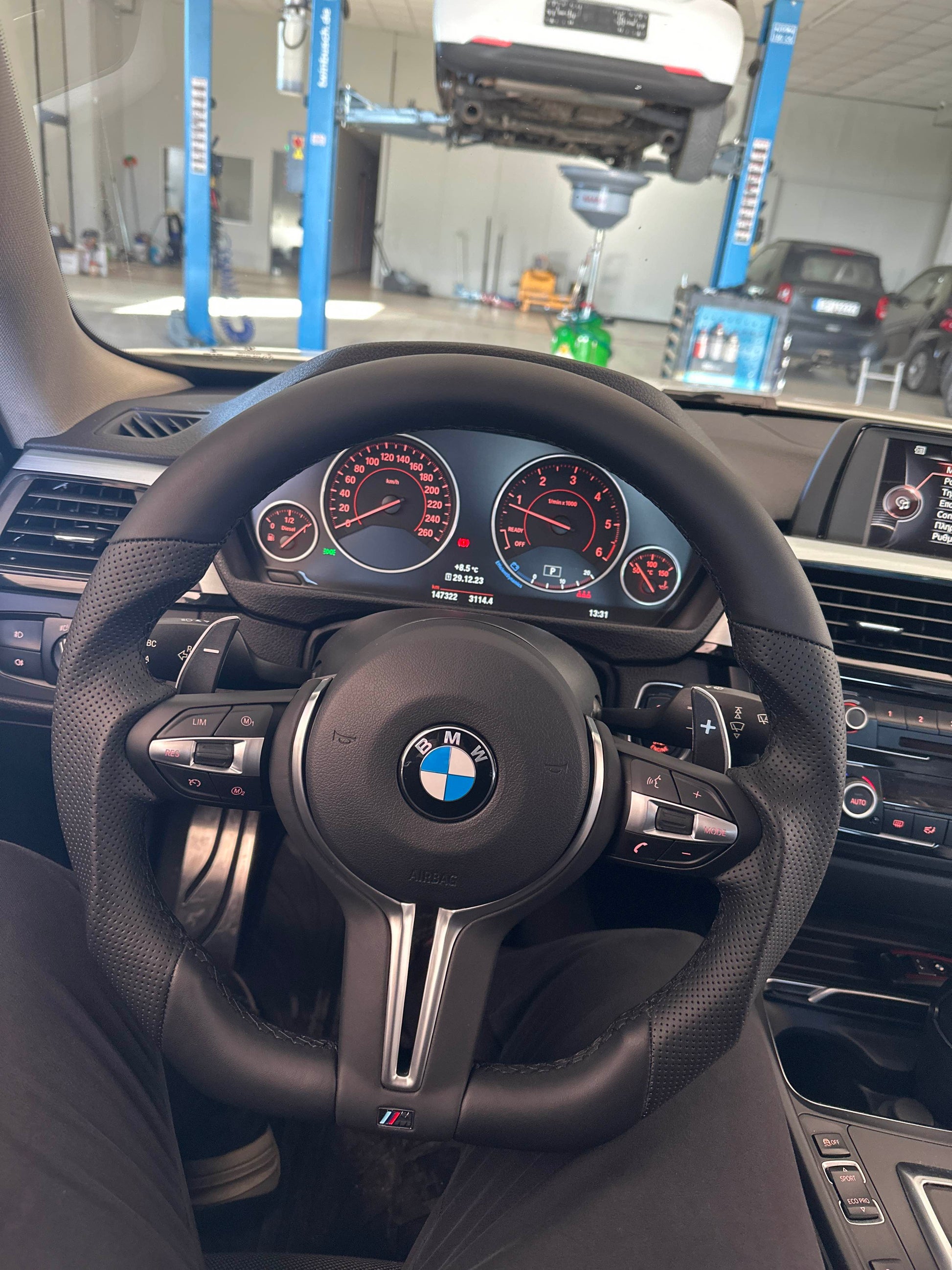 Steering wheel with BMW logo in a car interior, with a service counter in the background.