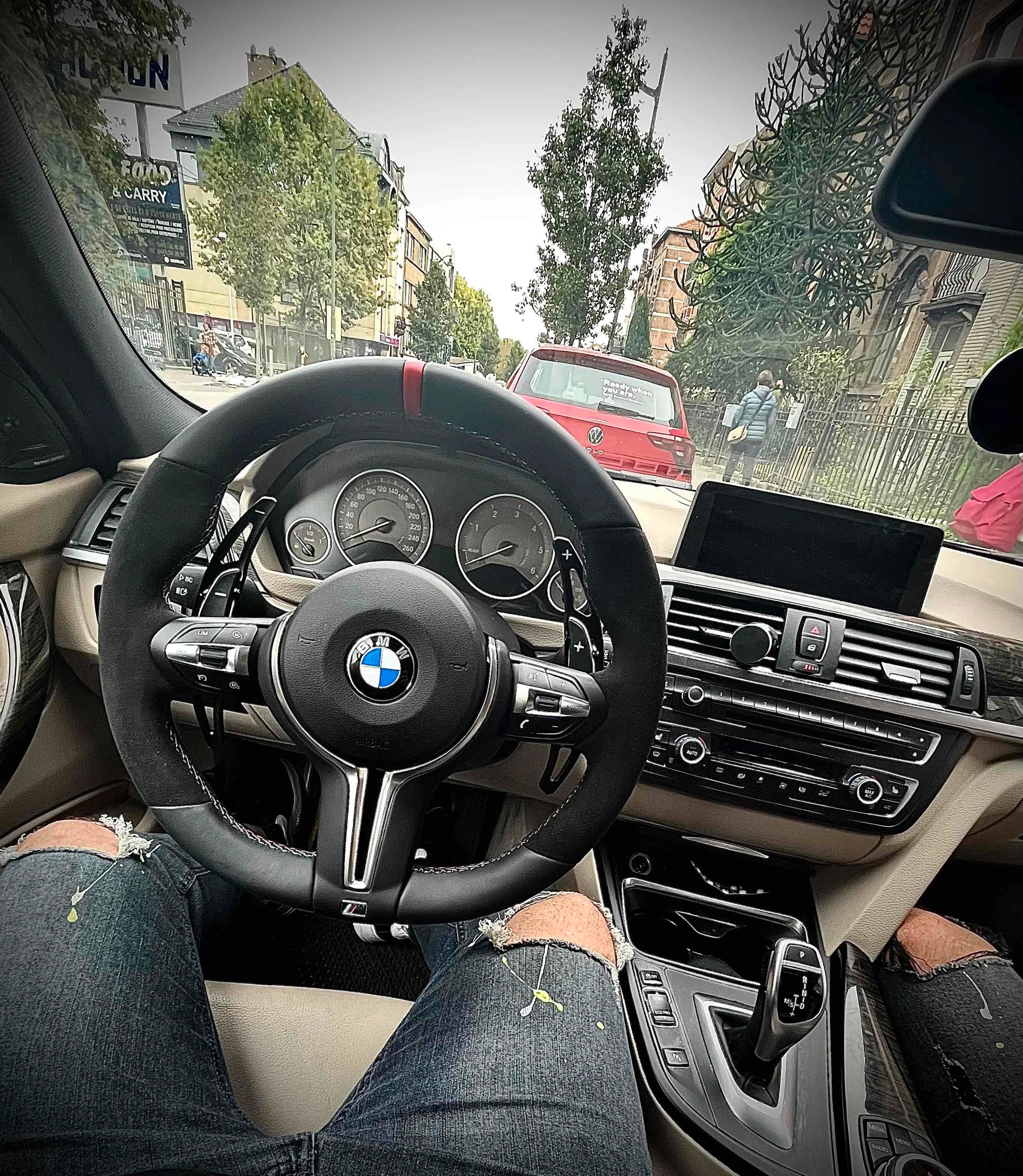 Car interior with a BMW steering wheel on a city street.
