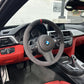 Car interior with steering wheel featuring BMW logo, red accents, and dashboard details.