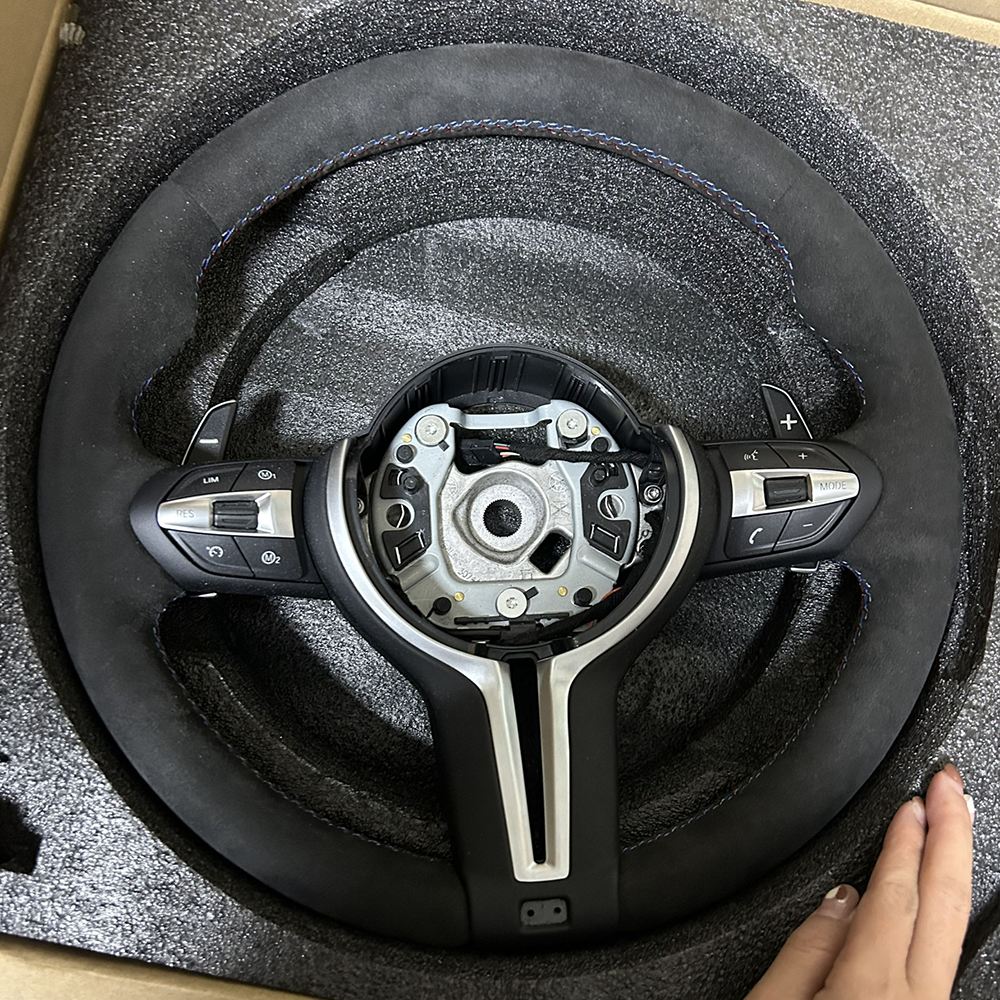 Custom BMW carbon steering wheel with black suede grip and blue stitching in protective foam packaging